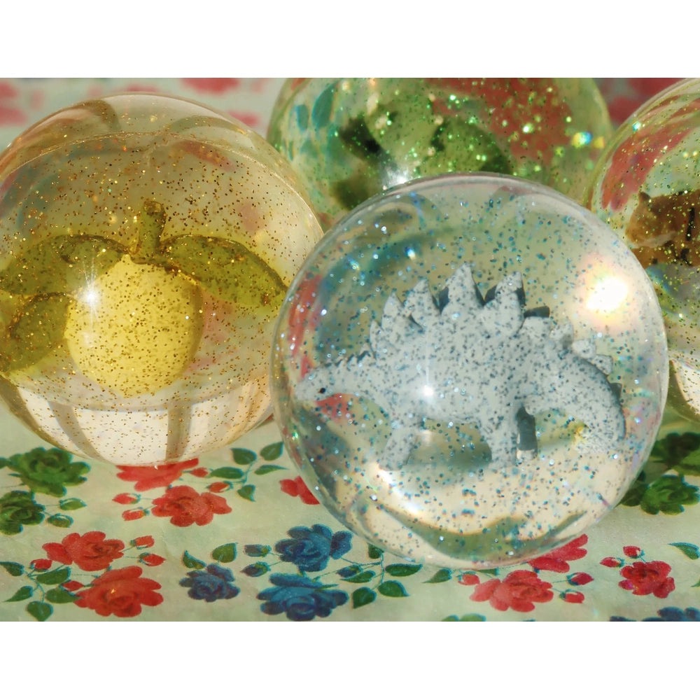 Konges Slojd Glitter Bouncing Ball Set Dino; glittery translucent spheres with dinosaur silhouette bouncing on a floral table.