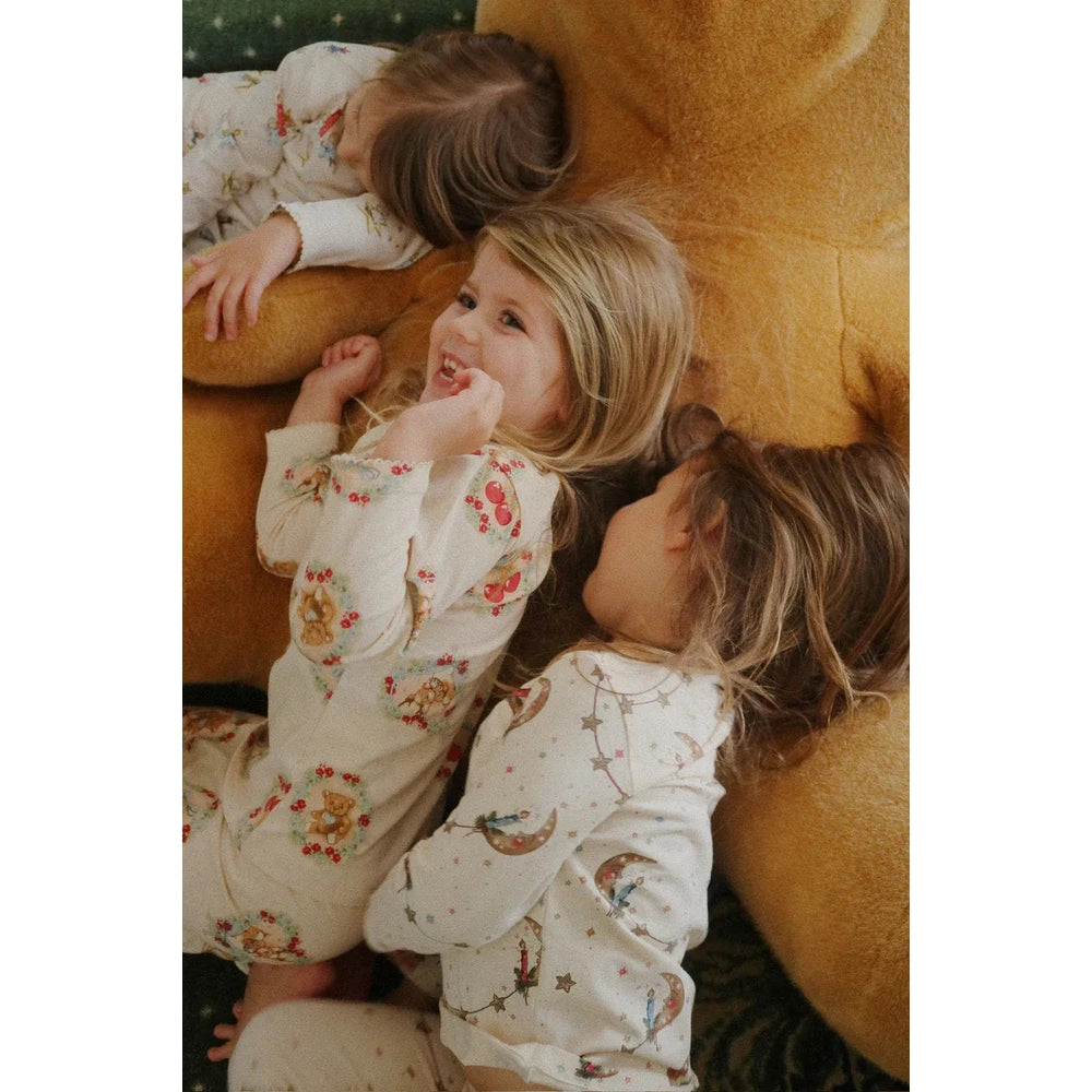 Konges Slojd Holiday Basic Blouse/Pants Set GOTS Deer Diary, cream sleepwear with deer print, worn by a smiling toddler resting on a plush teddy.