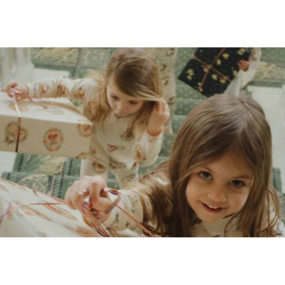 Konges Slojd Holiday Basic Blouse/Pants Set Gots Deer Diary worn by two smiling toddlers in cream deer-print pajamas while unwrapping gifts.