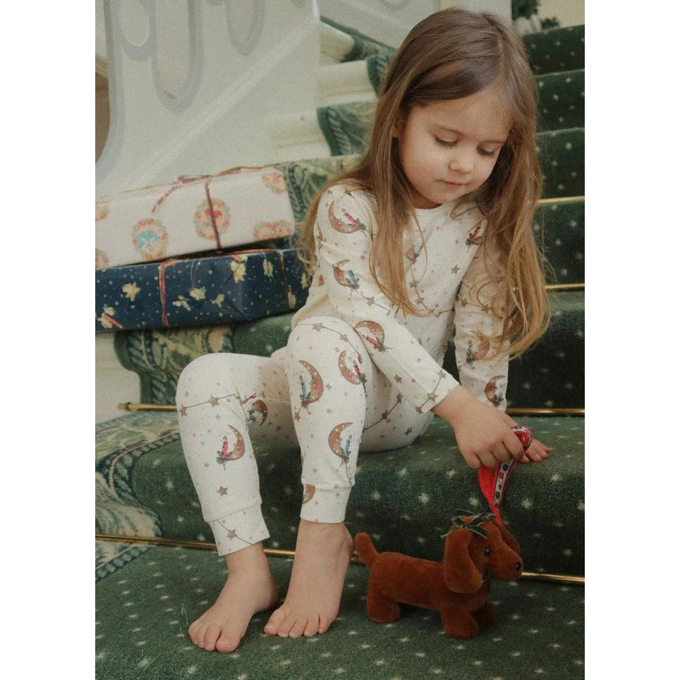 Konges Slojd Holiday Basic Blouse/Pants Set Gots Luna: girl in white moon/star pajamas playing with a brown plush dog on green carpet stairs.