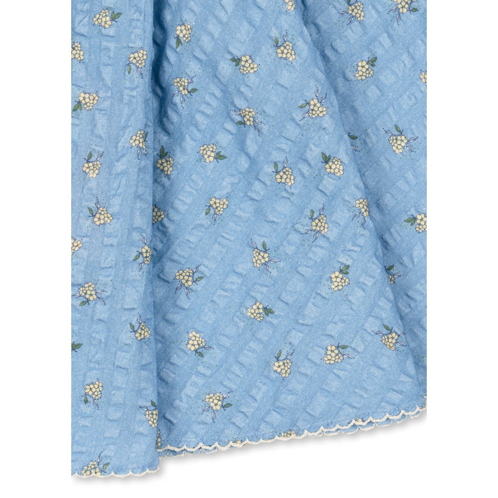 Konges Slojd Kim Skirt Billie Blue baby skirt laid flat to show blue fabric, tiny yellow flowers, and scalloped trim.