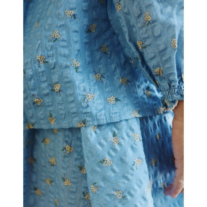 Konges Slojd Kim Skirt Billie Blue: toddler wearing light blue fabric with tiny white flower clusters, hand at side.