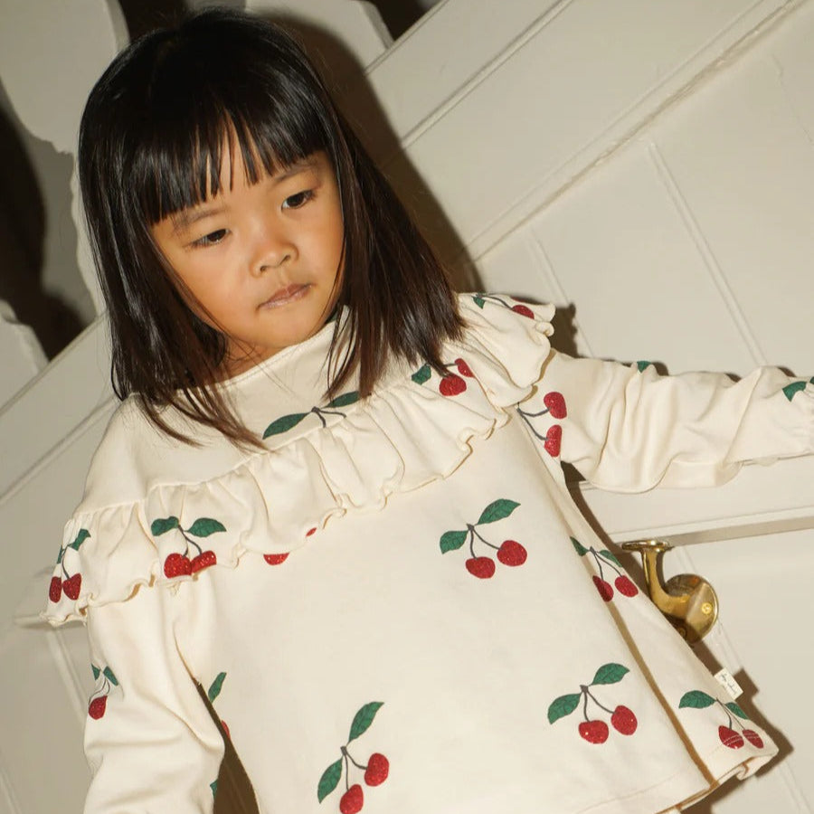 Konges Slojd Malli Glitter Blouse; cream with cherry print and ruffled yoke, worn by a young girl.