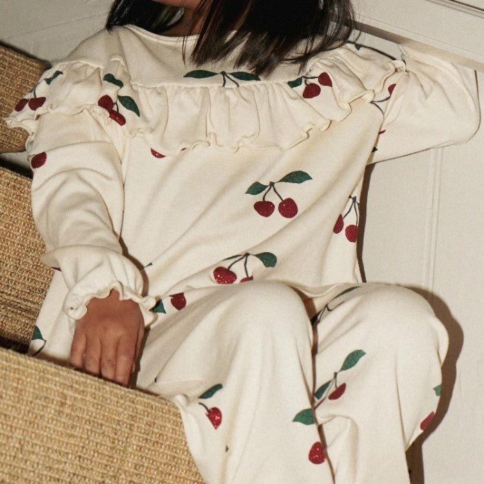 Konges Slojd Malli Glitter Blouse worn by a toddler; cream top with cherry prints, ruffled neckline, elastic cuffs.