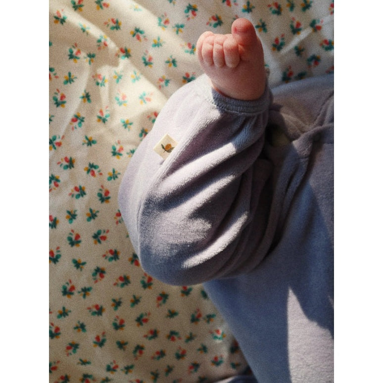 Konges Slojd Miffa Onesie Gots Trade Winds lavender, baby kicking leg to reveal soft knit fabric.