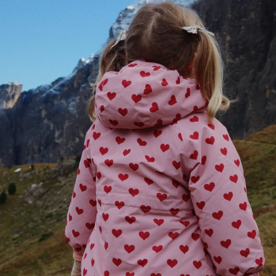 Konges Slojd Mismou Jacket Amour Pink worn by a child outdoors in a mountain landscape, pink heart-print coat with hood.