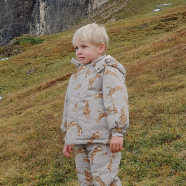 Konges Slojd Mismou Jacket Tiger Oak worn by a toddler standing on a grassy hillside, grey with tiger print.