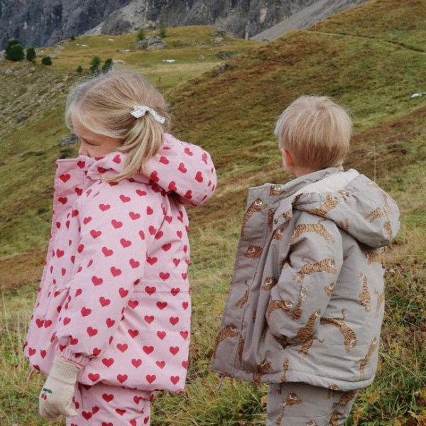 Konges Slojd Mismou Jacket Tiger Oak; two toddlers in heart-printed pink and tiger-pattern gray coats explore a hillside.