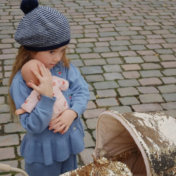 Konges Slojd Soleil Cardigan in country blue; blue knit baby top worn by a child holding a doll.