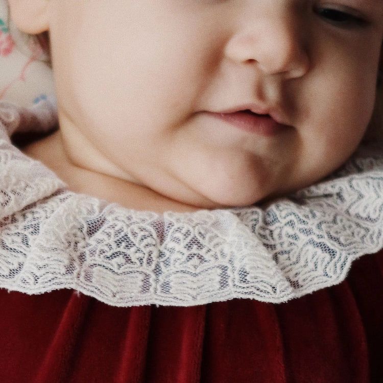 Konges Slojd Venola Romper Red Dahlia on a baby, burgundy velvet with a delicate white lace collar.