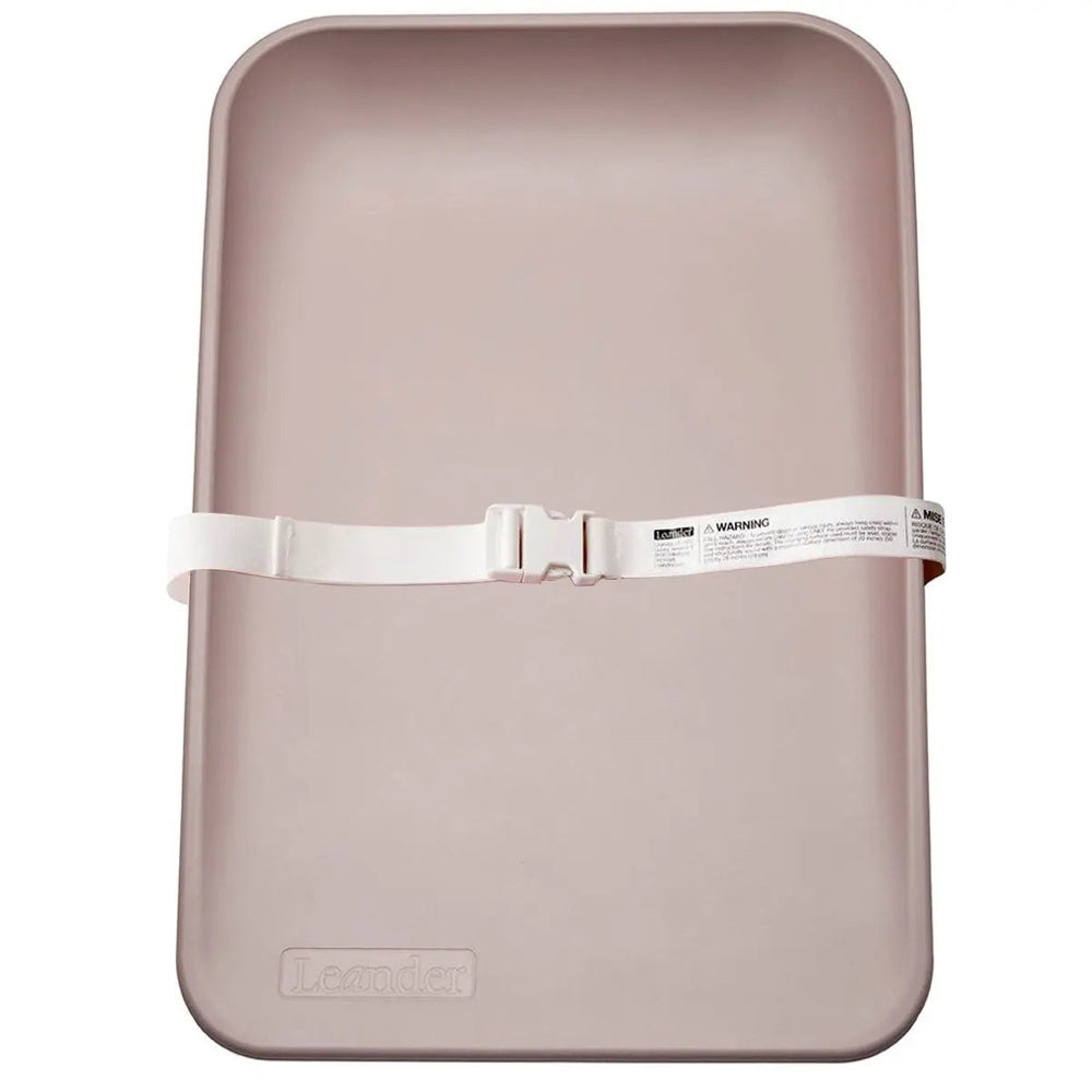 Leander Matty Changer changing mat in blush pink with a white safety strap securing it.