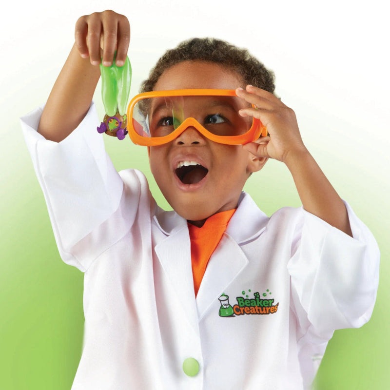 Learning Resources Breaker Creatures Lab Gear: child in white lab coat and orange goggles holds up a green creature.