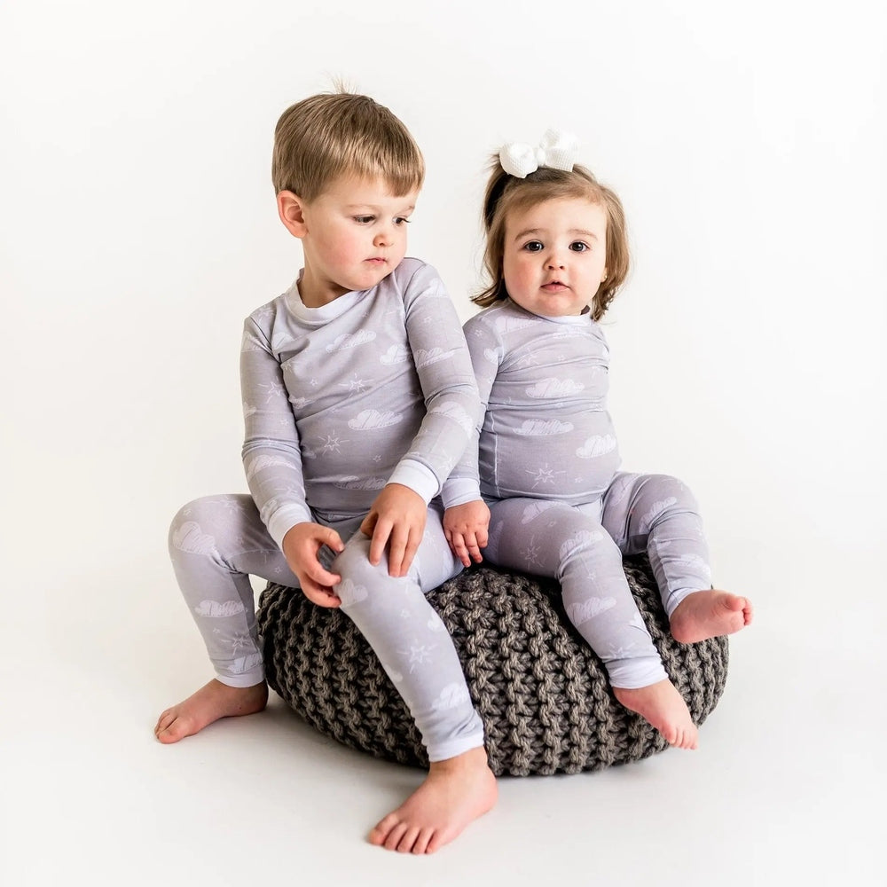 Little Sleepies Bamboo Pajama Set Clouds, gray bamboo fabric, two toddlers sit barefoot on a chunky knit pouf.