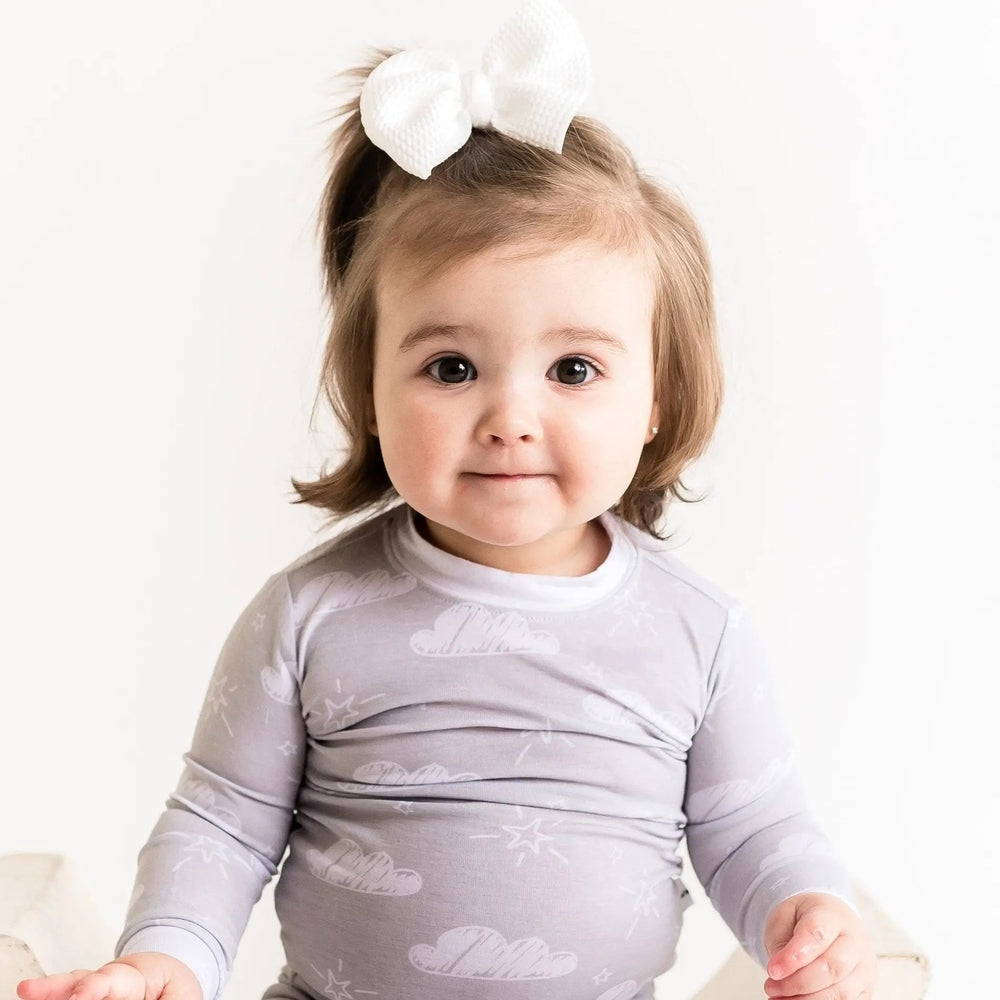 Little Sleepies Bamboo Pajama Set Clouds: baby in gray cloud-print long-sleeve onesie with white bow headband.
