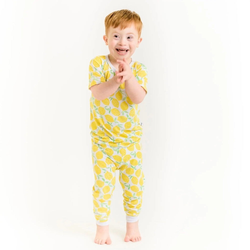Little Sleepies Bamboo Pajama Set Lemons worn by a joyful toddler in a lemon-print yellow two-piece set, clapping.