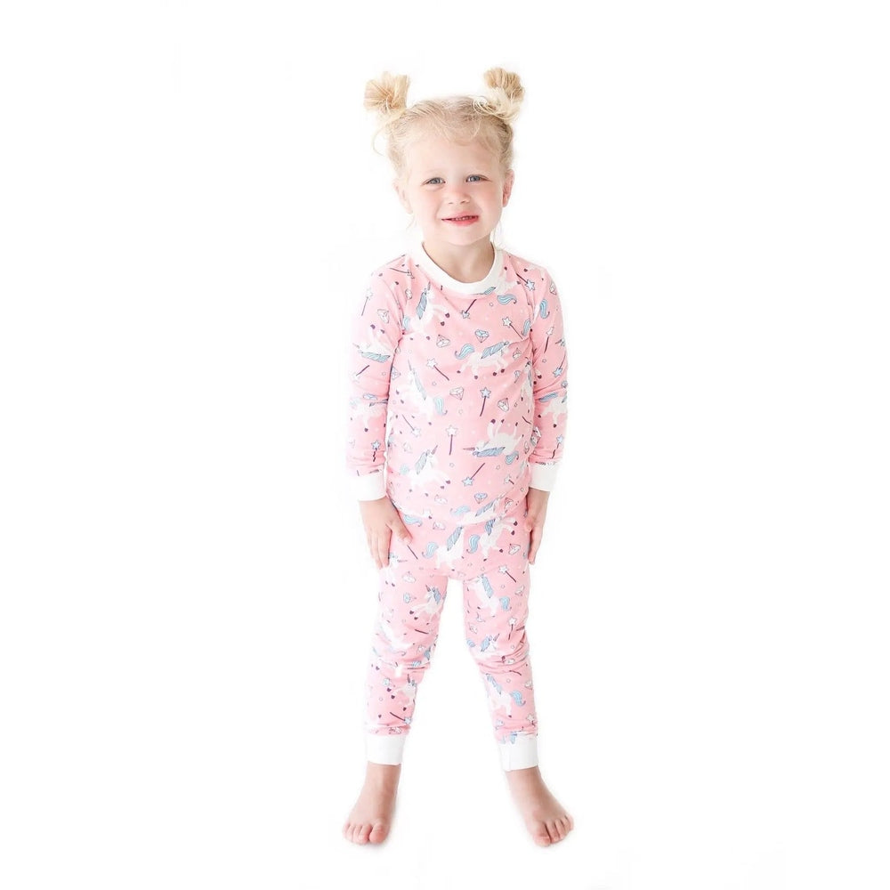 Little Sleepies Bamboo Pajama Set Pink Unicorn; toddler girl stands in pink unicorn-print sleepwear with white cuffs.