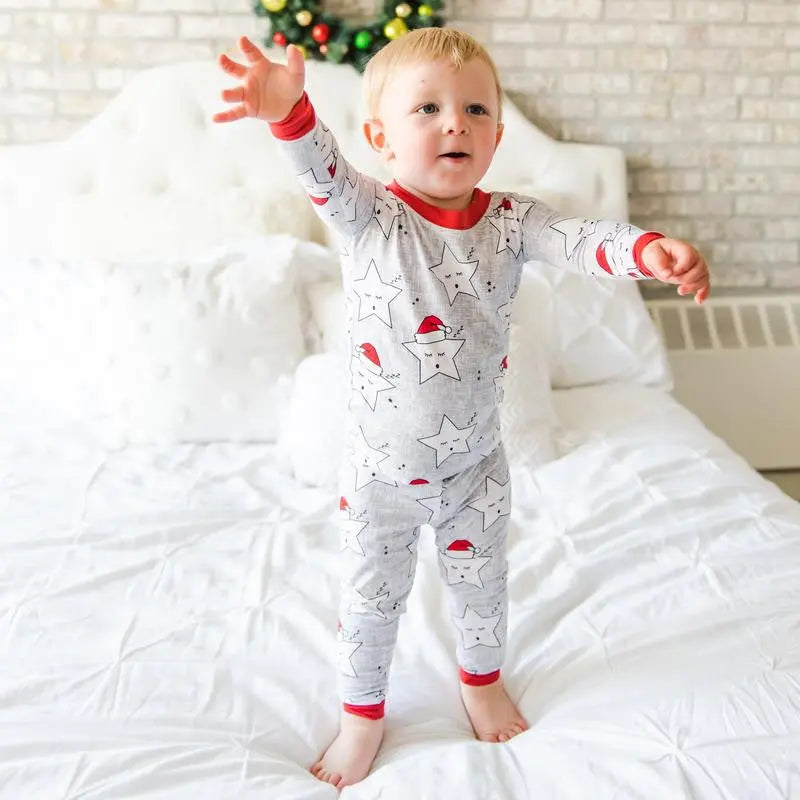 Little Sleepies Bamboo Pajama Set Santa Stars for toddlers, grey with star prints and red cuffs, child stands on a bed with arms out.