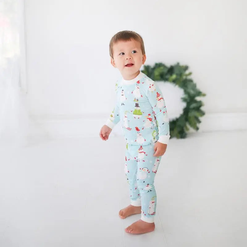 Little Sleepies Bamboo Pajama Set Snowman in light blue; toddler stands barefoot, highlighting soft, breathable bamboo fabric.