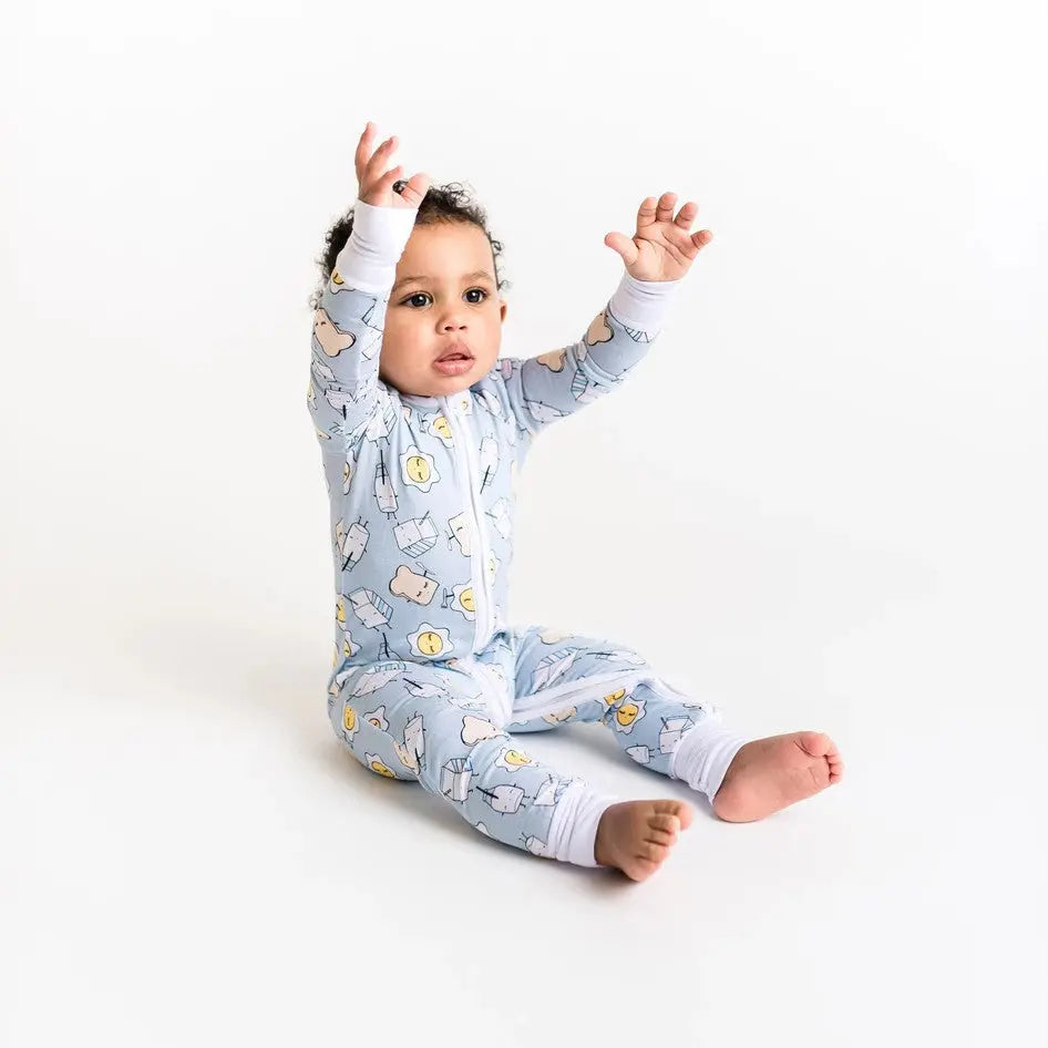 Little Sleepies Bamboo Zip Romper in Blue Breakfast print; baby sits with arms raised, zipper front.