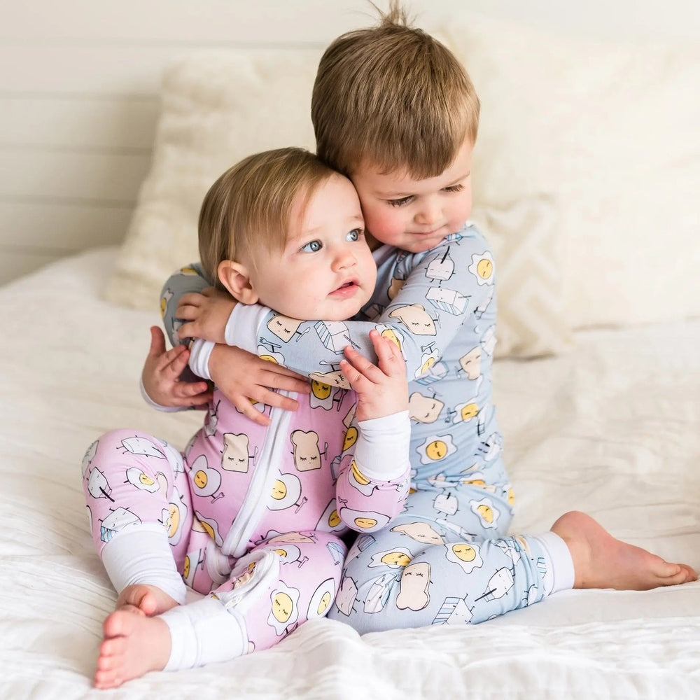 Little Sleepies Bamboo Zip Romper Sleeper Blue Breakfast; two babies cuddle on a bed, showing soft fabric and visible front zipper.