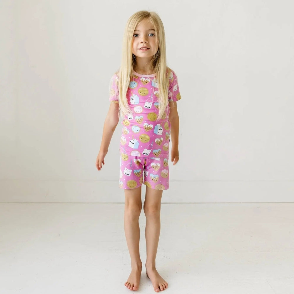 LITTLESLEEPIES pink cookies & milk two-piece pajama set with short sleeves and shorts in bamboo viscose, worn by a girl.