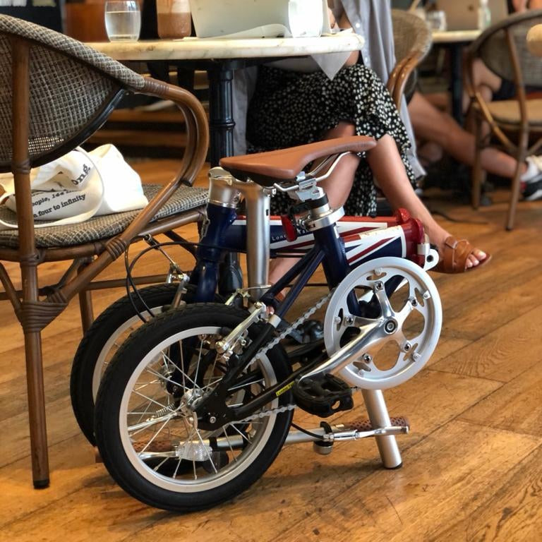 London Taxi folding 14-inch aluminum lightweight bicycle with brown saddle in cafe setting