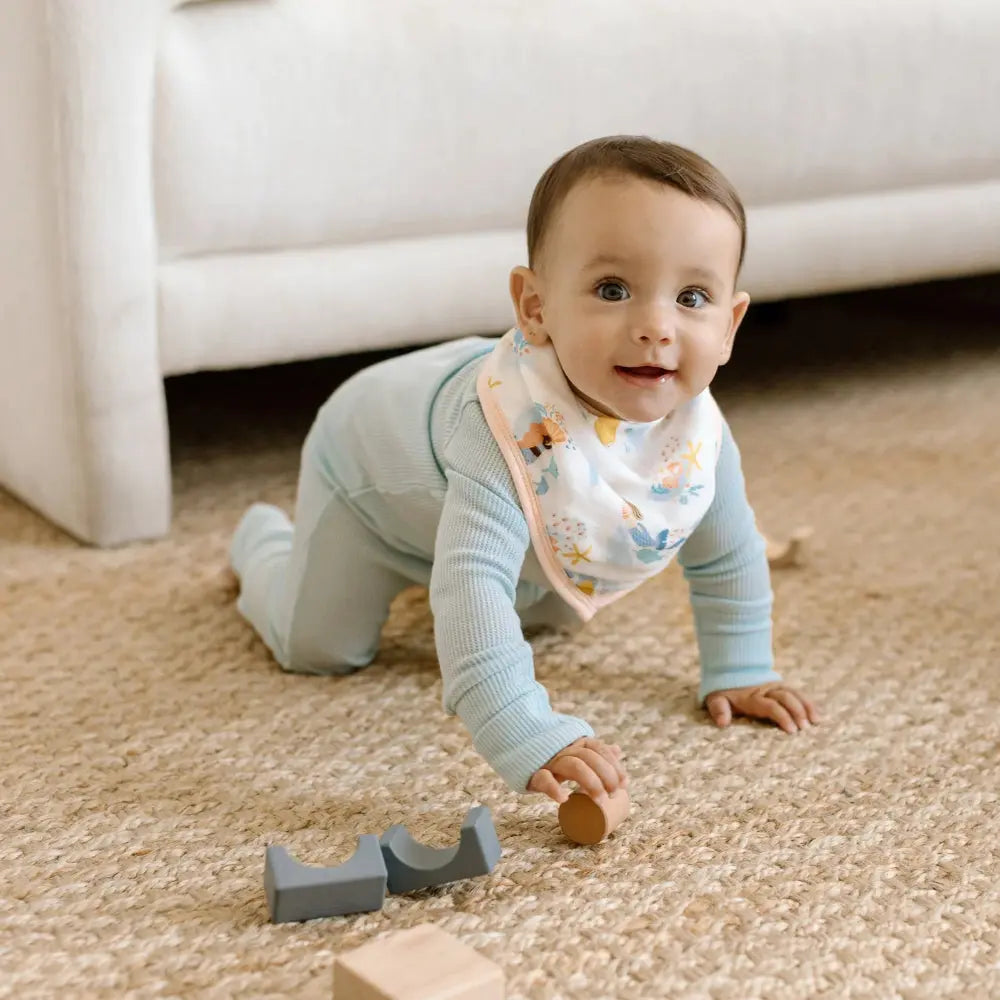 Loulou Lollipop Bandana Bib Set on a crawling baby in pastel blue, reaching for wooden blocks.