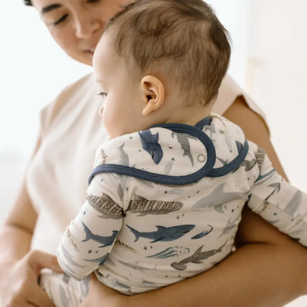 Loulou Lollipop Bandana Bib Set with navy trim; baby in ocean-print bib being fed by caregiver.