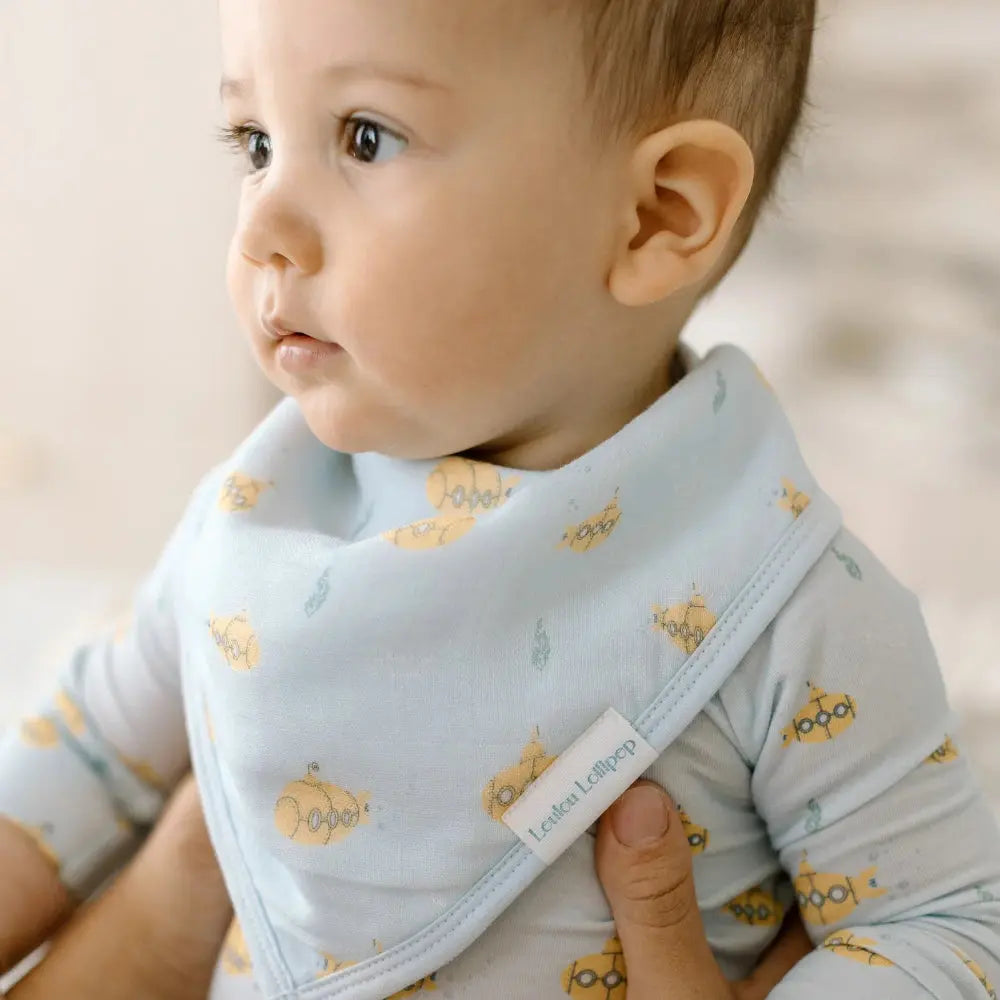 Loulou Lollipop Bandana Bib Set, light-blue with yellow submarine prints, worn by a baby during feeding.