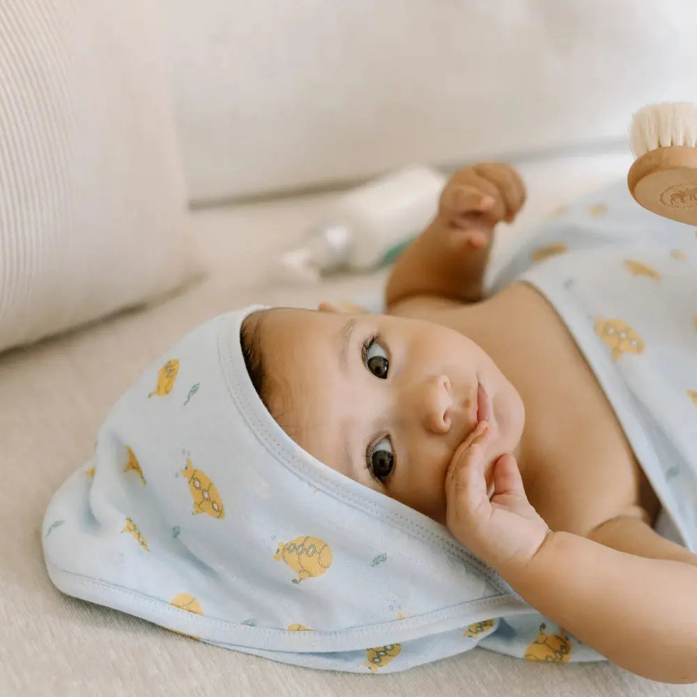 Loulou Lollipop Hooded Towel Set: light-blue hooded towel with yellow prints, baby lying post-bath with hand to face.