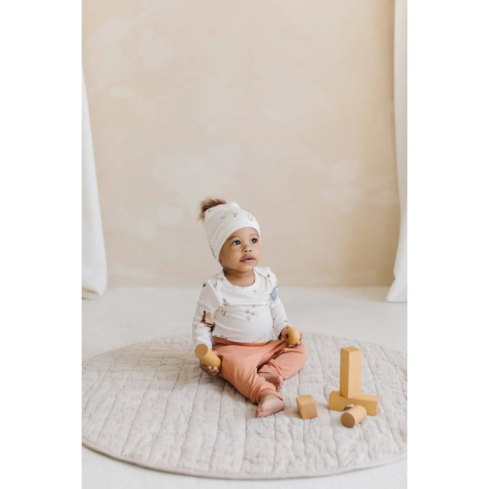 Loulou Lollipop Long Sleeve Bodysuit Cozy Forest; white with forest print, baby sits on a quilted rug playing with wooden blocks.