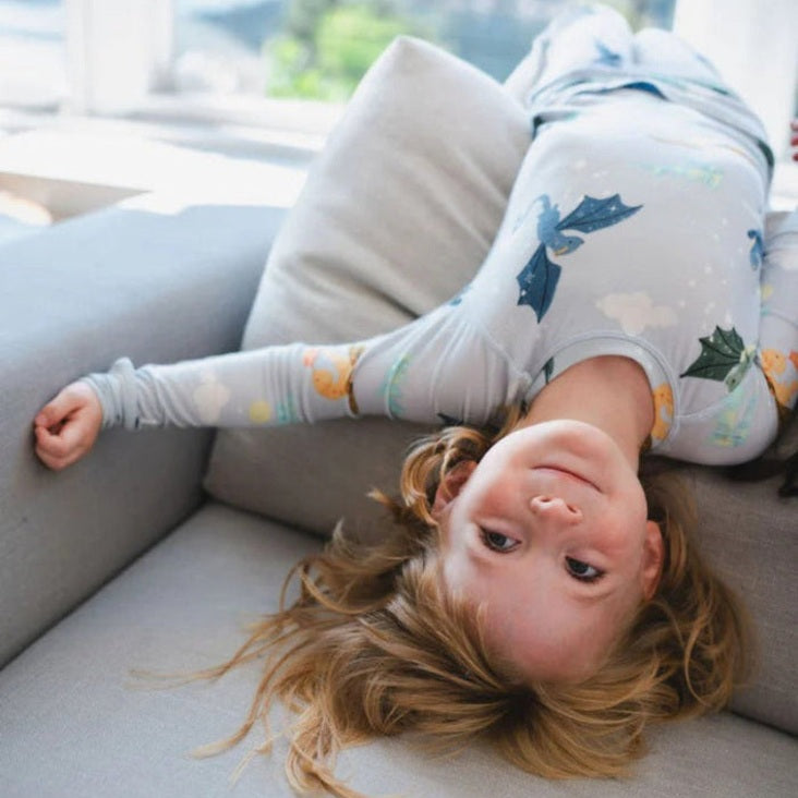 Loulou Lollipop Long Sleeve Pajama Set Magical Dragons: child lounging upside-down on a sofa in light-blue dragon-print sleepwear.
