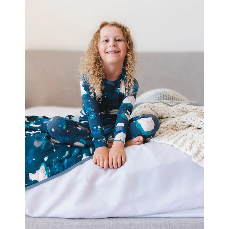 Loulou Lollipop Long Sleeve Pajama Set Stargazing Bear in blue starry print, worn by a smiling child sitting on a bed.