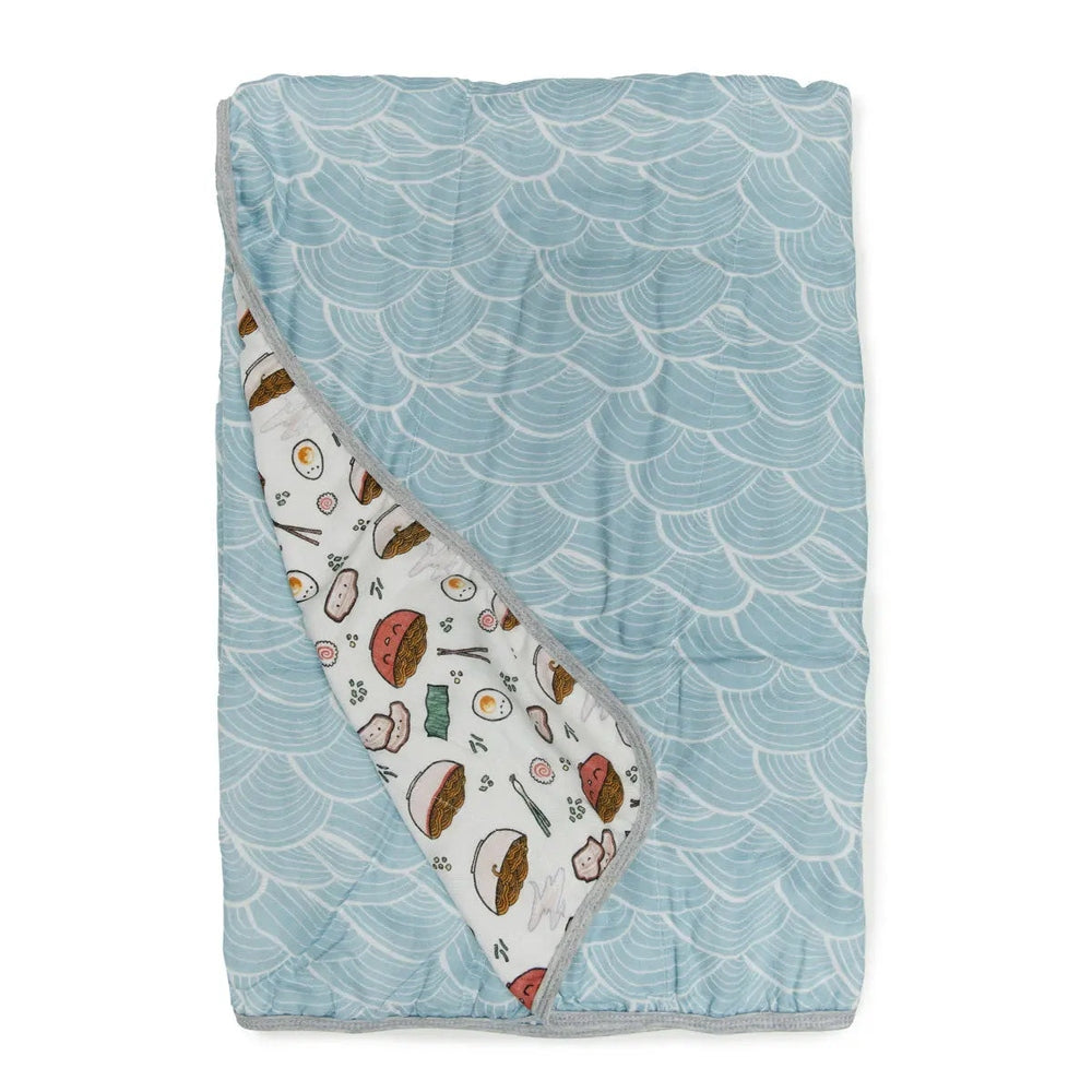 Loulou Lollipop Muslin Quilt Blanket, light blue wave exterior with a corner turned to reveal the food-themed interior.