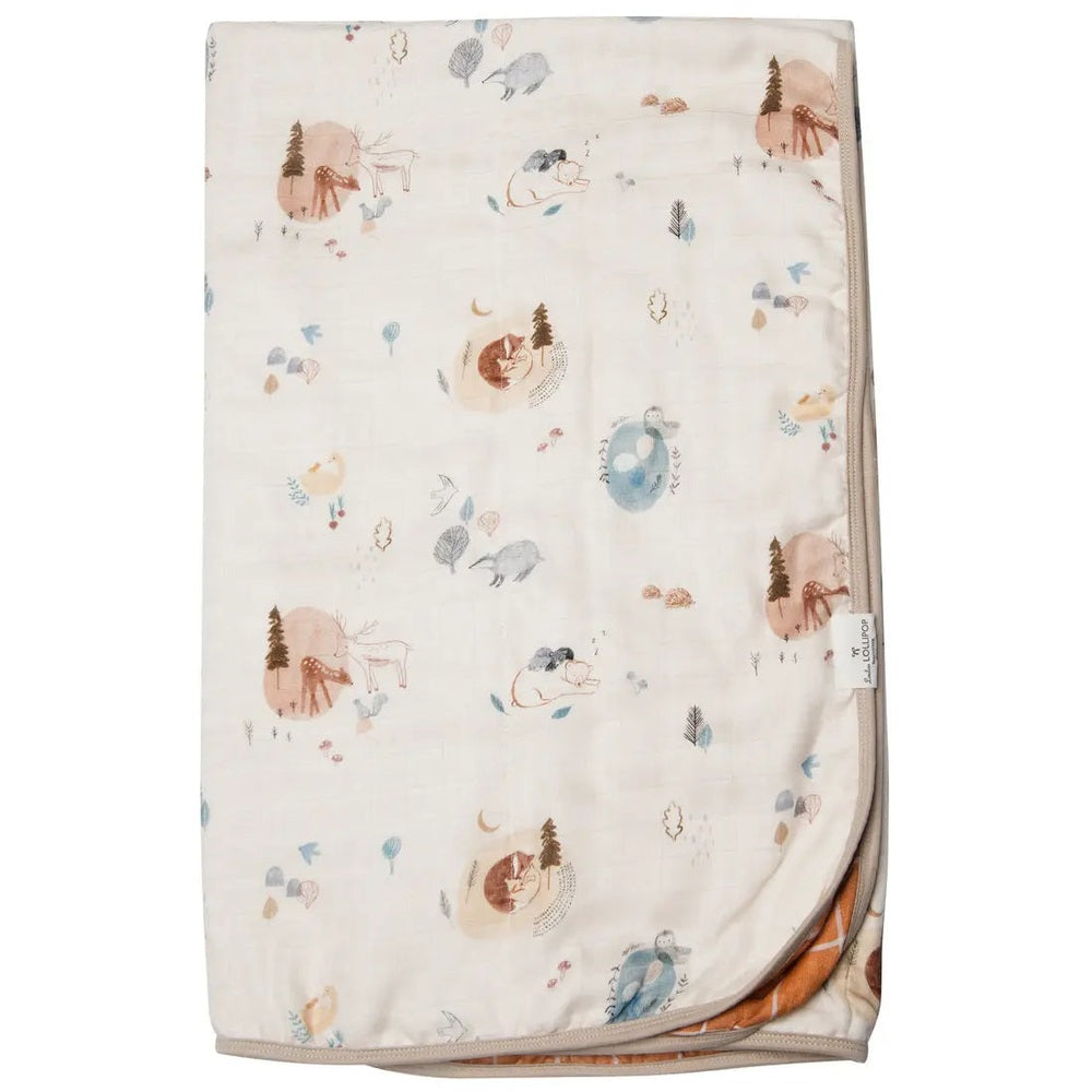 Loulou Lollipop muslin quilt blanket in cream with woodland animals, folded to reveal a soft orange reverse.