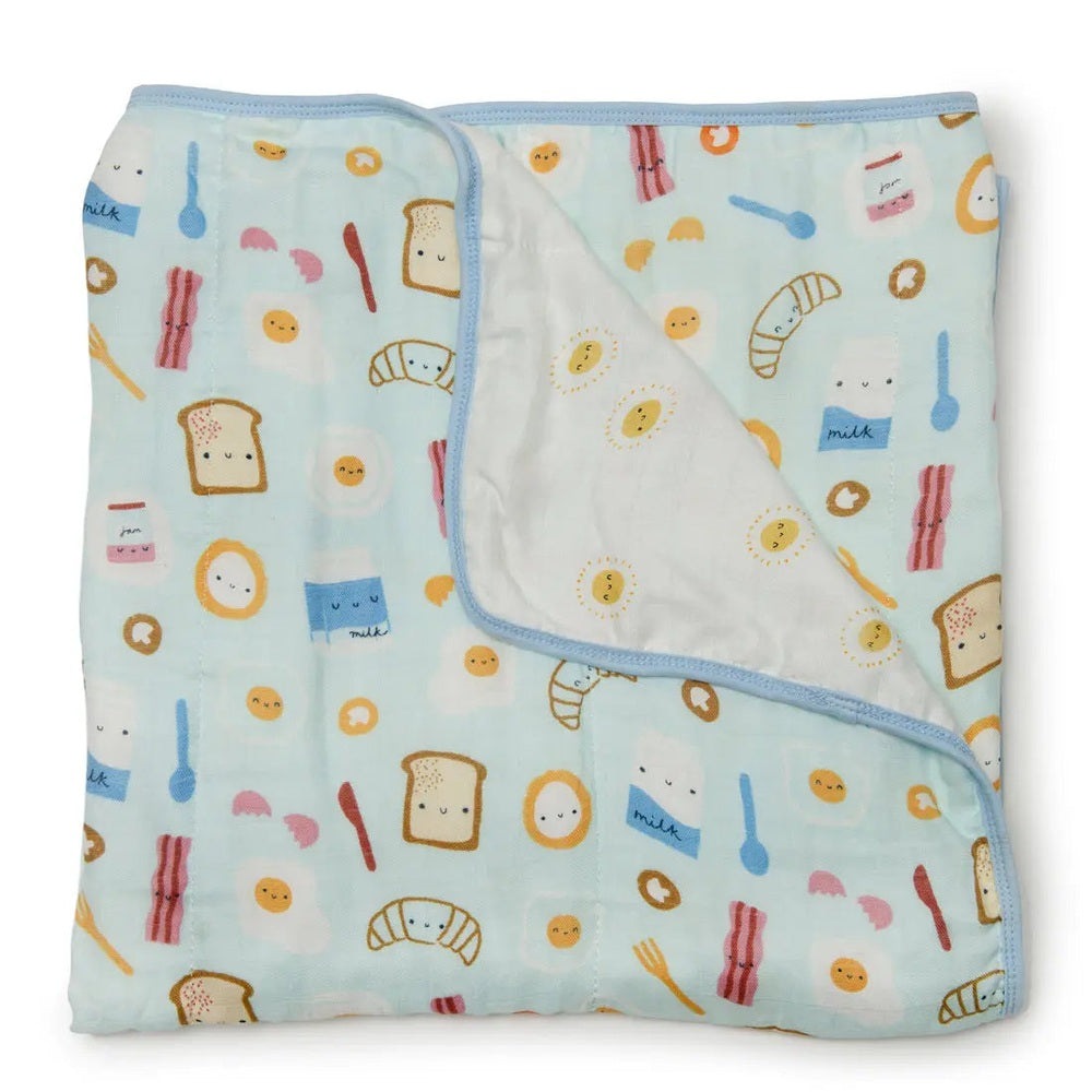 Loulou Lollipop Muslin Quilt Blanket in pastel blue, folded open to show white reverse with sunny motifs.