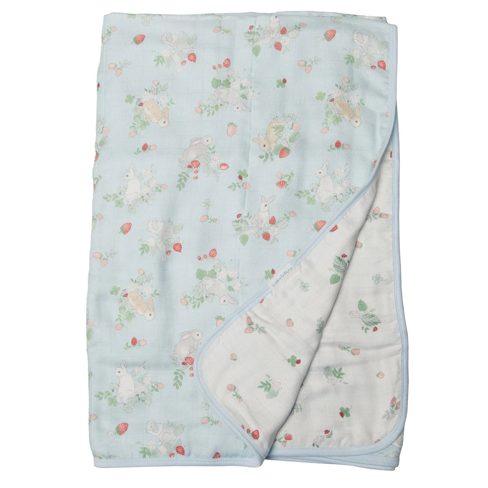 Loulou Lollipop Muslin Quilt Blanket in pale blue, folded to reveal the soft muslin side with bunny and strawberry print.