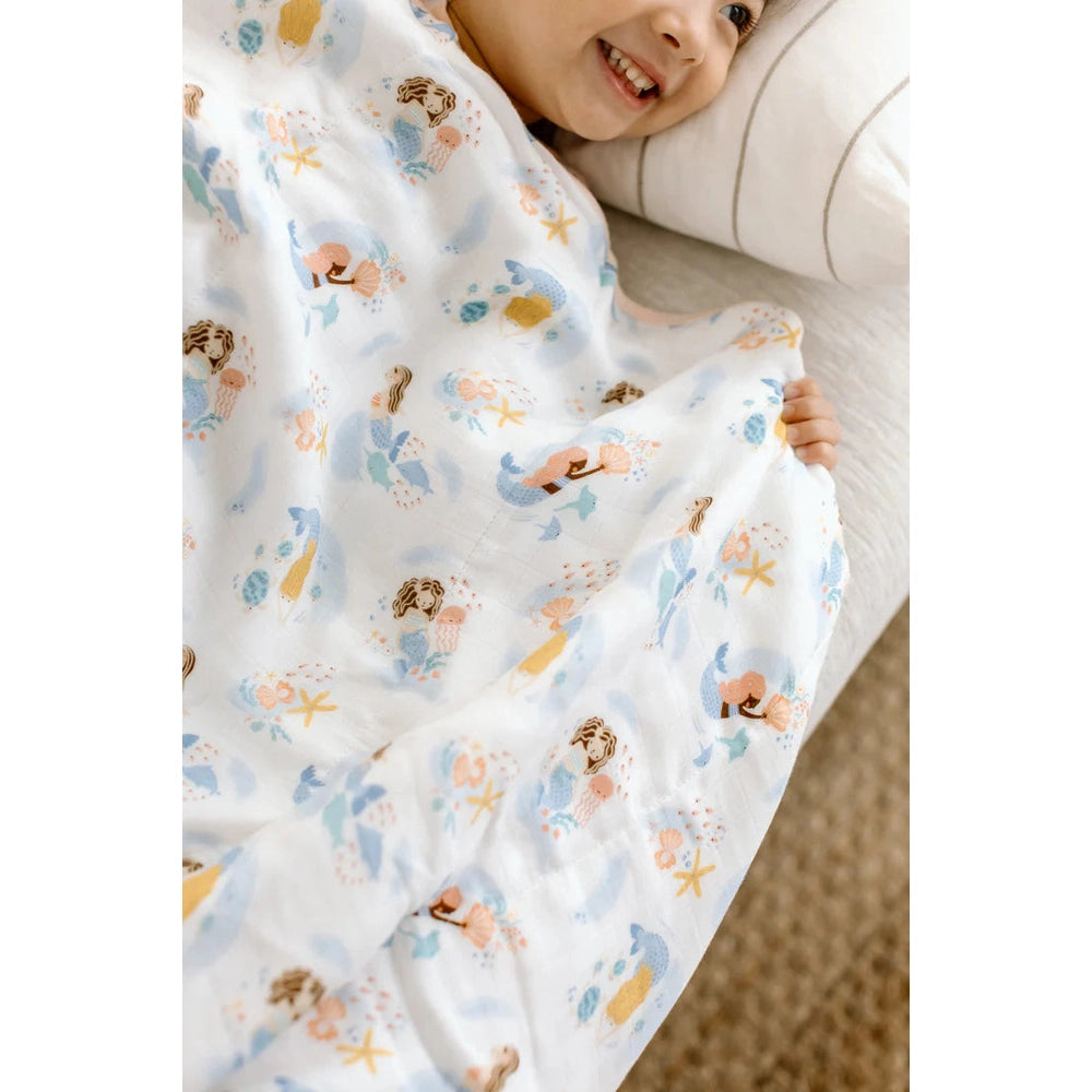 LOULOU LOLLIPOP Muslin Quilt Blanket swaddles a smiling toddler in pastel sea-print fabric.
