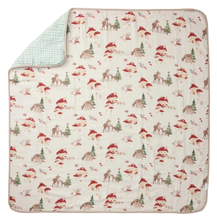 LOULOU LOLLIPOP Muslin Quilt Blanket with woodland print of deer and red mushrooms; mint backing shows at folded corner.