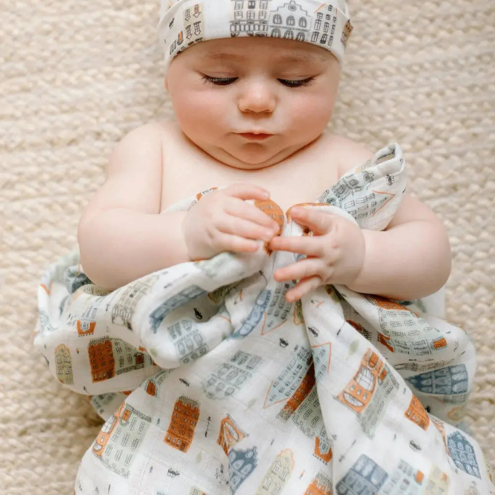 Loulou Lollipop Muslin Swaddle in city-print, baby snugly wrapped and gently holding the fabric.