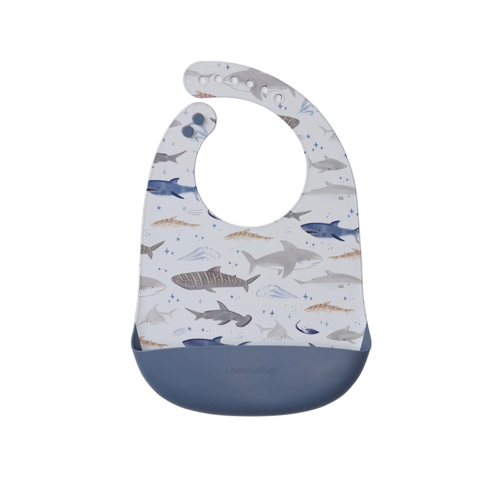 Loulou Lollipop Silicone Bib with blue pocket, shark-print front, shown catching crumbs at mealtime.