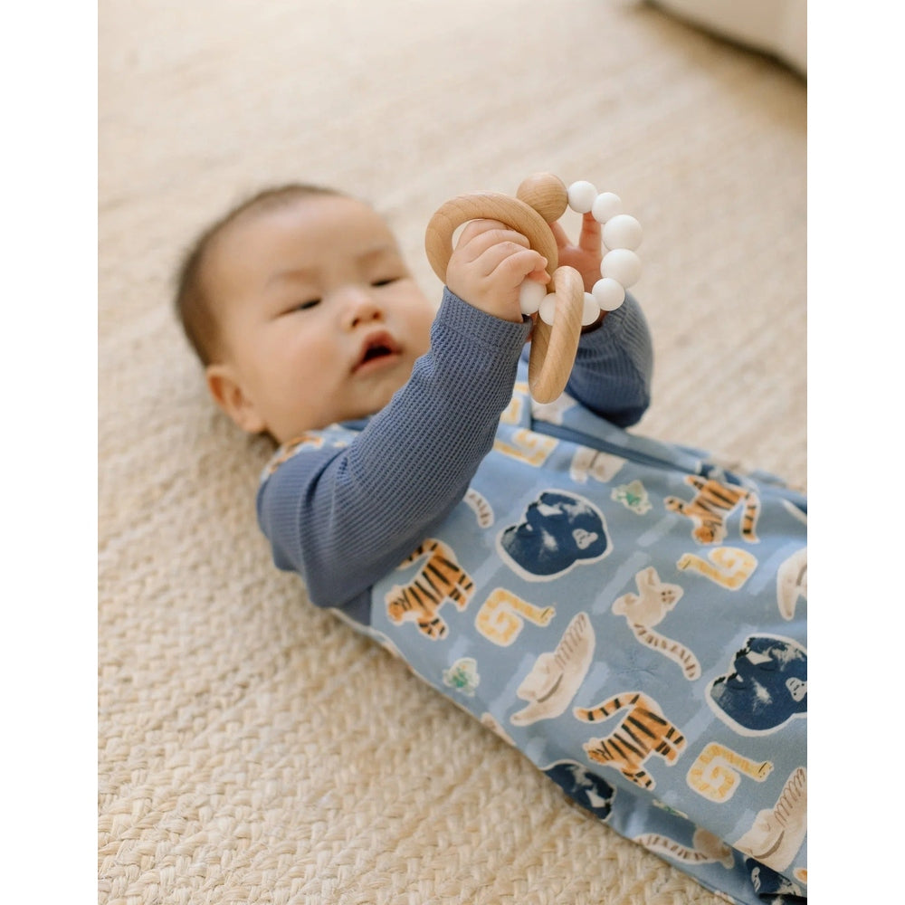 Loulou Lollipop TENCEL Sleep Bag 1.0 TOG Jungle Friends in blue; baby lies on a rug, gripping a wooden teether.