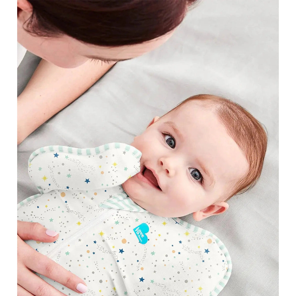 Love To Dream Swaddle Up Organic Cotton 0.2 Tog Cream Constellation baby swaddle; parent gently holds the baby's sides.