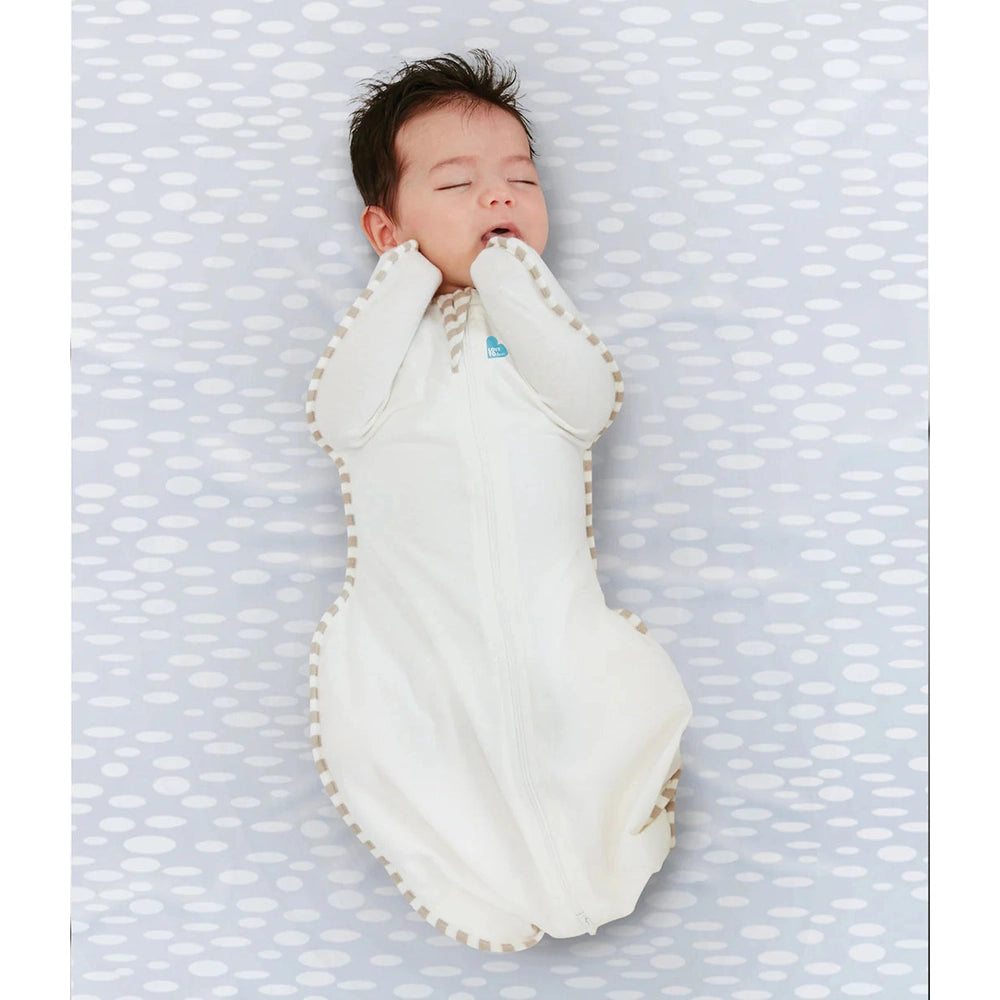 Love To Dream Swaddle Up Original Cotton 1.0 Tog cream swaddle with beige trim; baby sleeps with arms up in the zip.