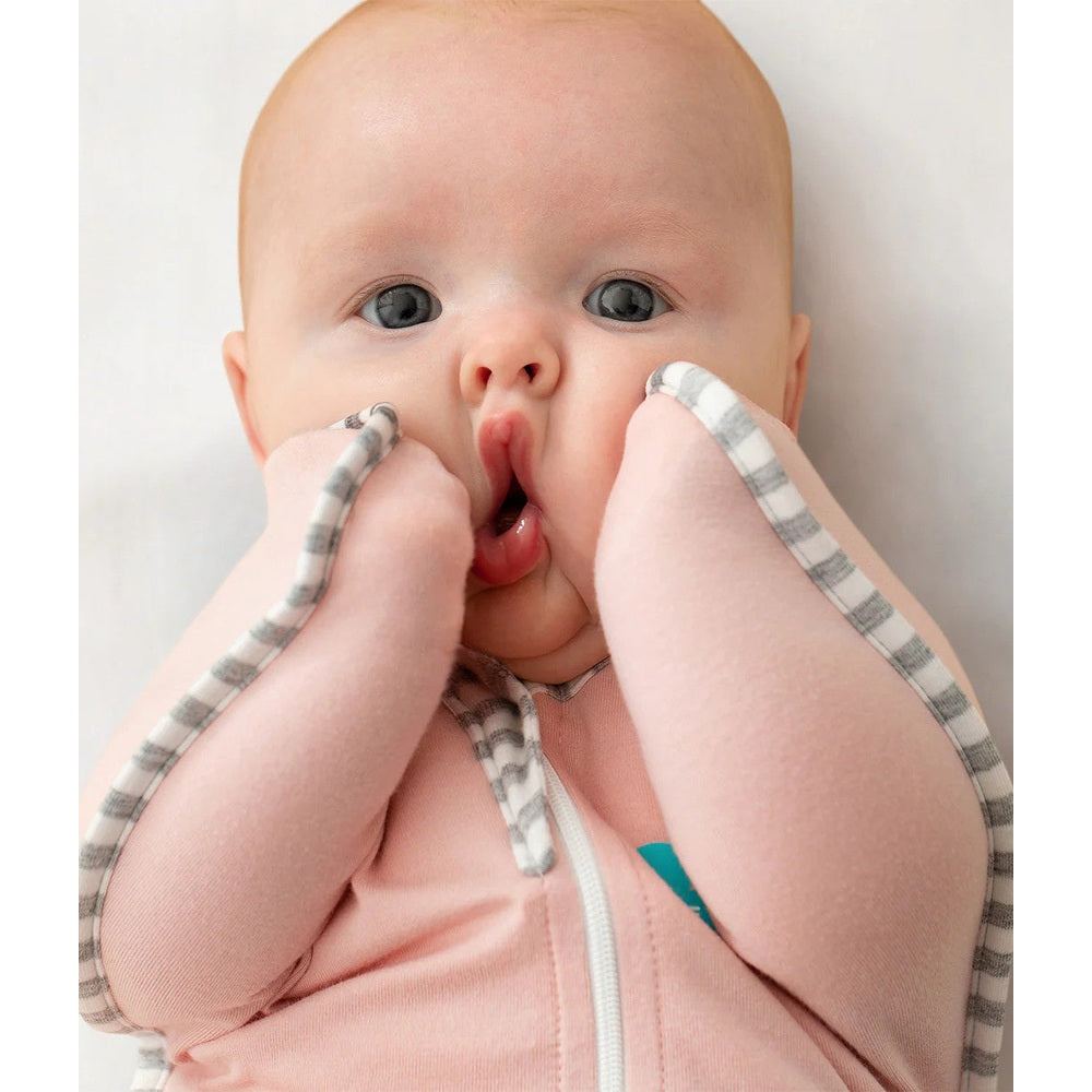 Love To Dream Swaddle Up Original Cotton 1.0 Tog Dusty Pink; pink zip-swaddle with striped cuffs, baby hands by face.