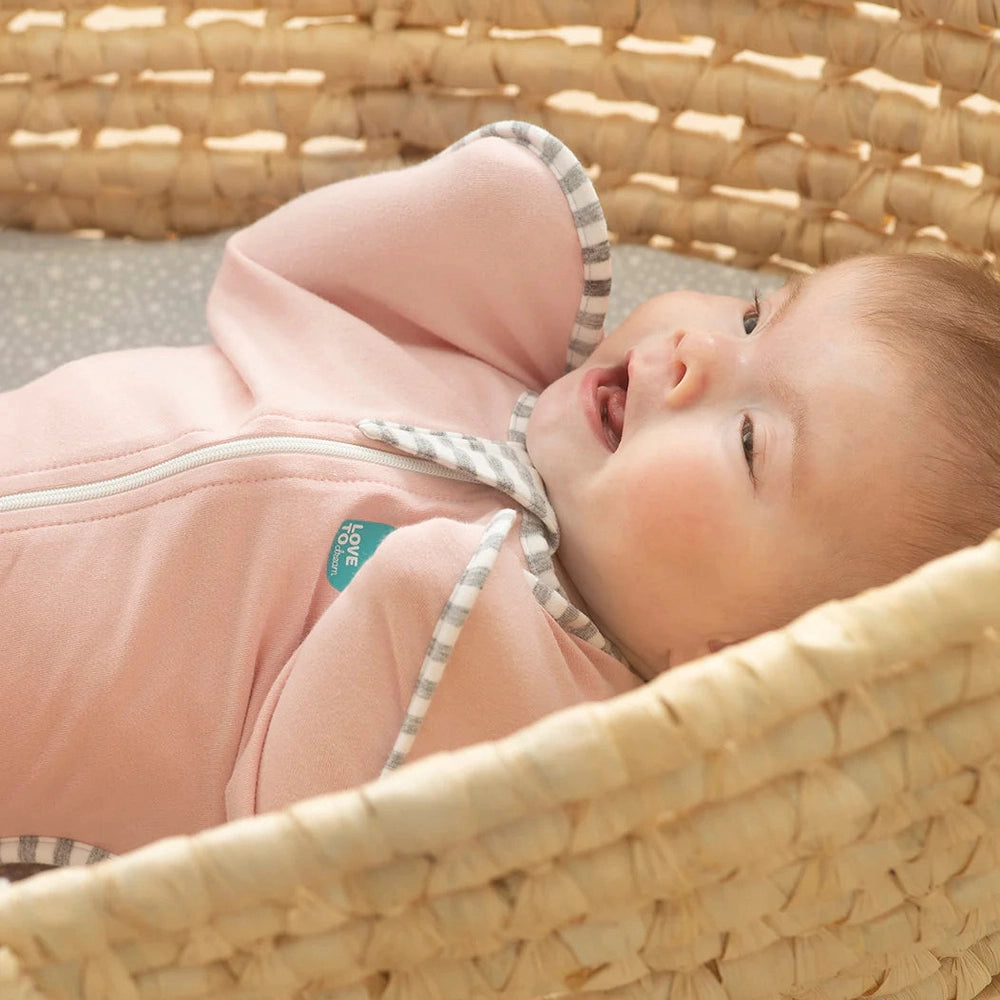 Love To Dream Swaddle Up Original Cotton 1.0 Tog Dusty Pink baby swaddle on a smiling infant in a woven basket with gray striped trim