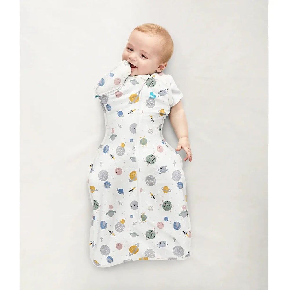 Love To Dream Swaddle Up Transition Bag Cotton 0.2 Tog White Space; baby lies calmly swaddled in space-print white sleepwear.