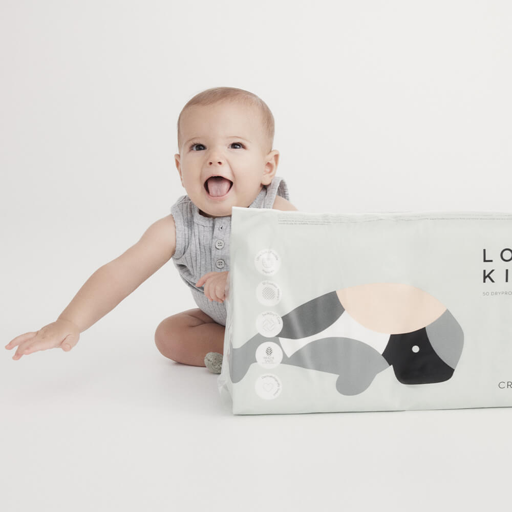 Lovekins DryProtect crawler nappies M (6–11kg) package beside smiling baby