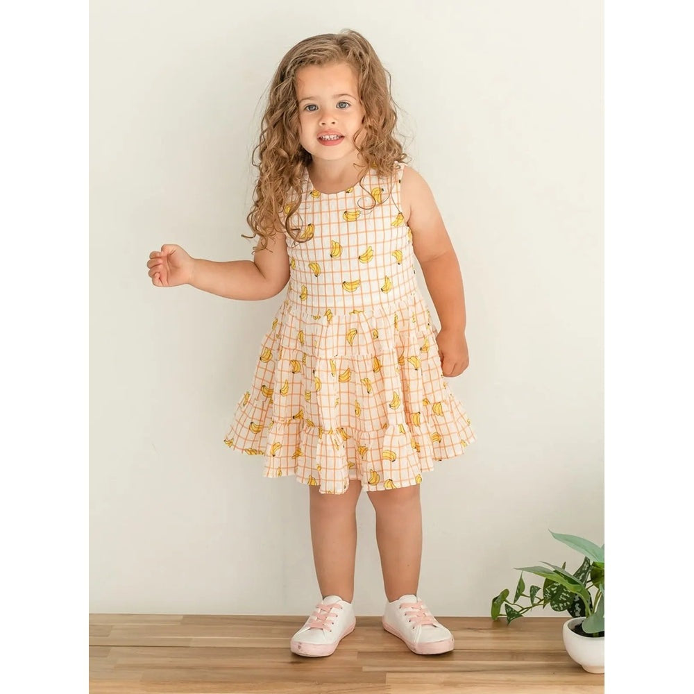 MABEL AND HONEY Bananas Printed Crinkle Chiffon Dress worn by a smiling girl, peach grid with banana print.