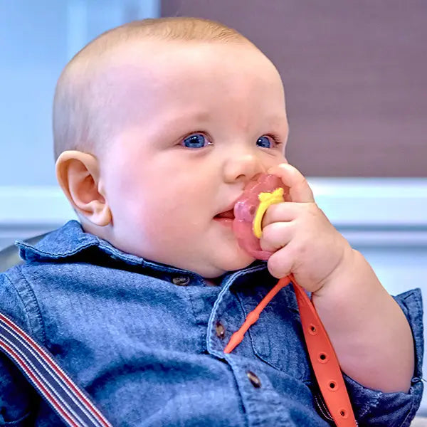 Marcus & Marcus Flip N' Strap feeding strap in orange; baby holds a pink pacifier attached to the strap.